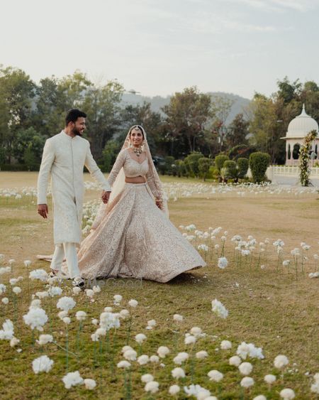 Gorgeous shot of the couple walking hand in hand between the aisle that is decorated with all-white floral single flower decor