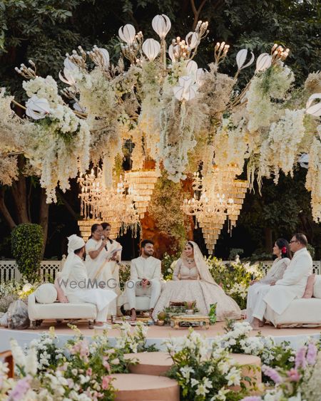 Super royal all-white mandap decor with florals and chandeliers, with female priestess conducting the wedding